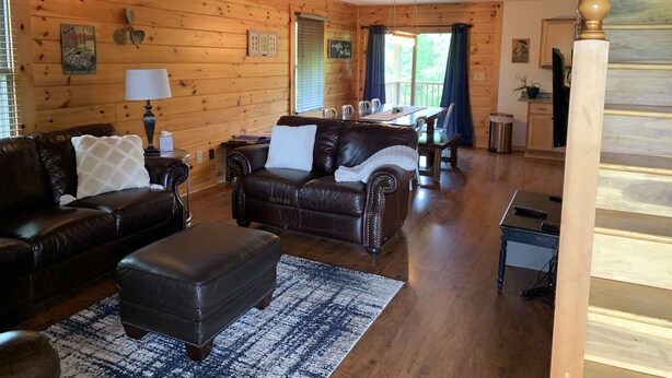 Un interior de cabaña acogedor, con paredes de madera, un comedor y una sala de estar con muebles de cuero.