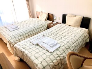 Two twin beds with checkered bedding, a bedside table with a lamp, and a chair. - Urban Times Hiroshima (Hiroshima)