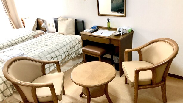 A hotel room with a bed, two chairs, a small table, a desk, a mirror, and a window with curtains. - Urban Times Hiroshima (Hiroshima)