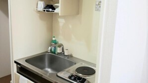 A compact kitchenette with a sink, stove, and storage shelves. - Urban Times Hiroshima (Hiroshima)