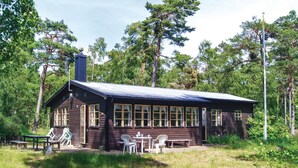 Une cabane rustique dotée d’une cheminée, de grandes fenêtres et d’une table de pique-nique avec des chaises.