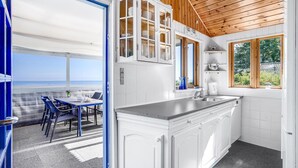 Une cuisine avec des meubles blancs, un évier et une fenêtre donnant sur une plage.