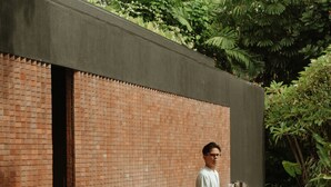 Un homme se tient près d’une fontaine, avec un mur de briques et de la verdure en arrière-plan.