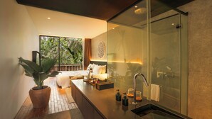 Une salle de bain moderne avec une douche à parois de verre, une grande plante en pot et une table de chevet avec une lampe.