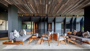Un salon moderne avec un plafond en bois, des canapés gris, des chaises en bois et une table basse.