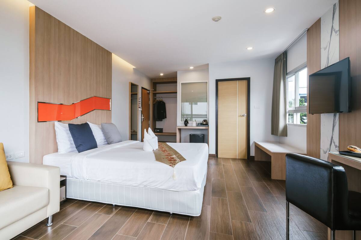 Quarto de hotel moderno com cama, escrivaninha, televisão e casa de banho visível através de uma porta aberta.