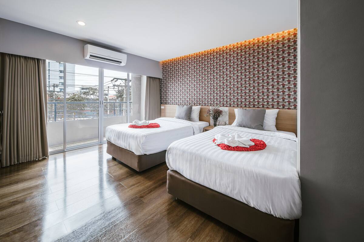 Quarto de hotel com duas camas, uma janela grande e parede com padrão.