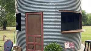 A cylindrical metal structure with a door and windows, surrounded by gravel and grass.