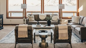 A cozy living room with a sofa, two armchairs, a coffee table, and a view of a lake through large windows.