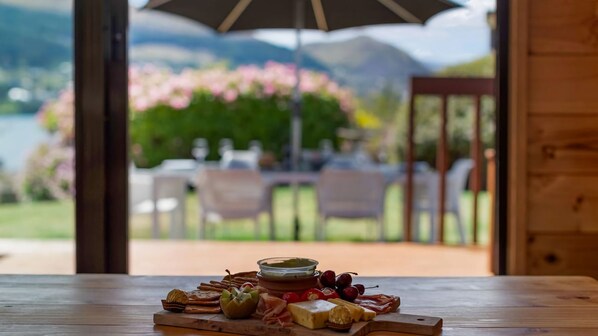 A wooden table with a charcuterie board and a view of a garden with chairs and tables outside.