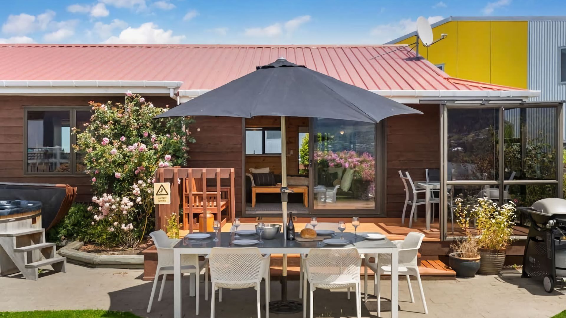 Eine Terrasse mit Tisch, Stühlen, einem Grill und einem Blumenstrauch.