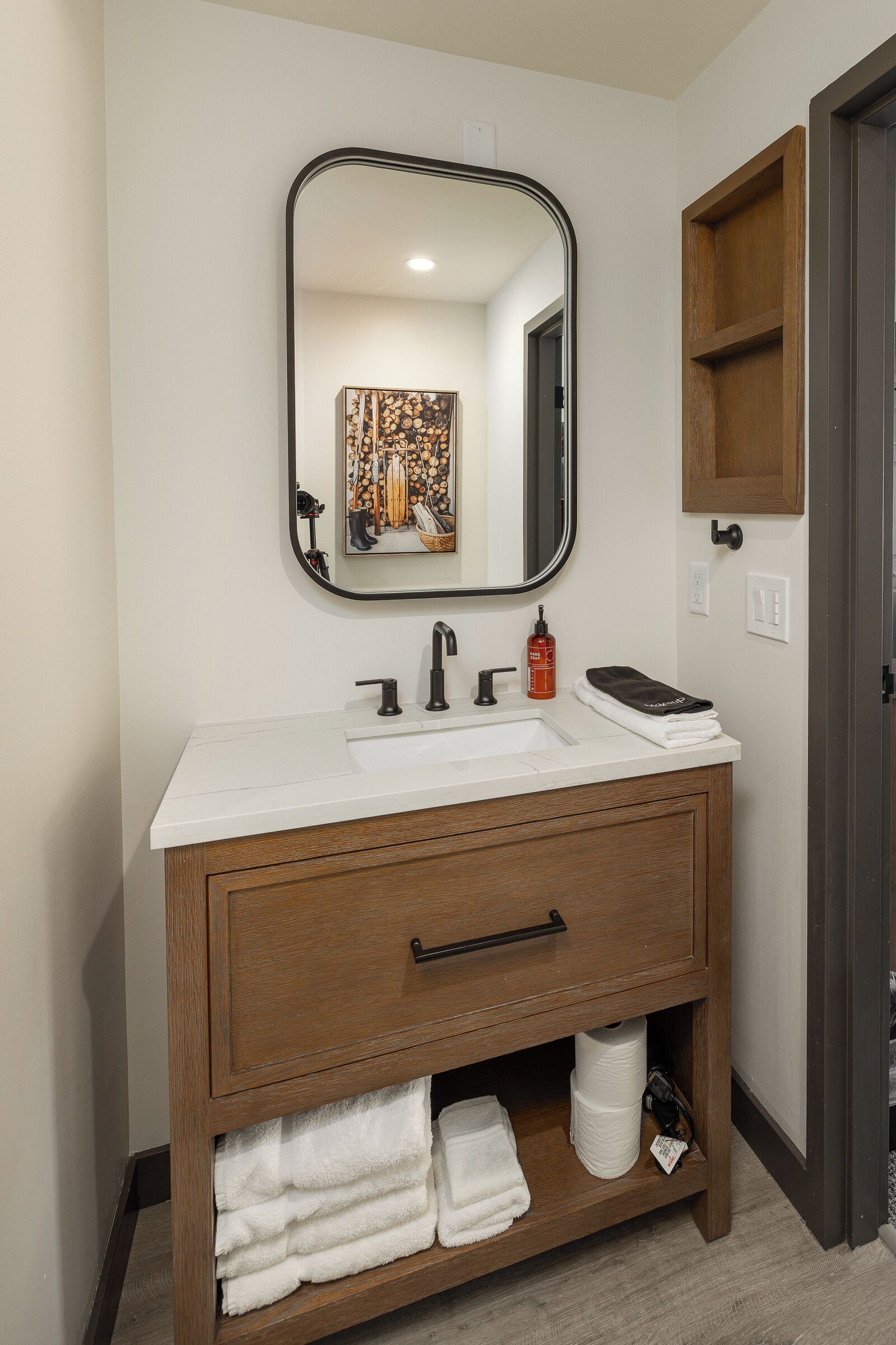 A bathroom with a white sink, wooden vanity, a mirror, and a towel rack.