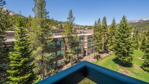 Un hôtel moderne à plusieurs étages, entouré d’une forêt dense et avec des montagnes en toile de fond.