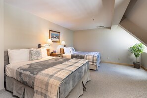 A hotel room with two beds, a painting on the wall, and a potted plant.