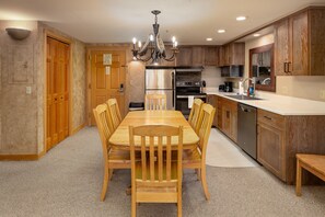 A modern kitchen with wooden cabinets, a stainless steel refrigerator, a built-in oven, and a dining area with a wooden table and chairs.