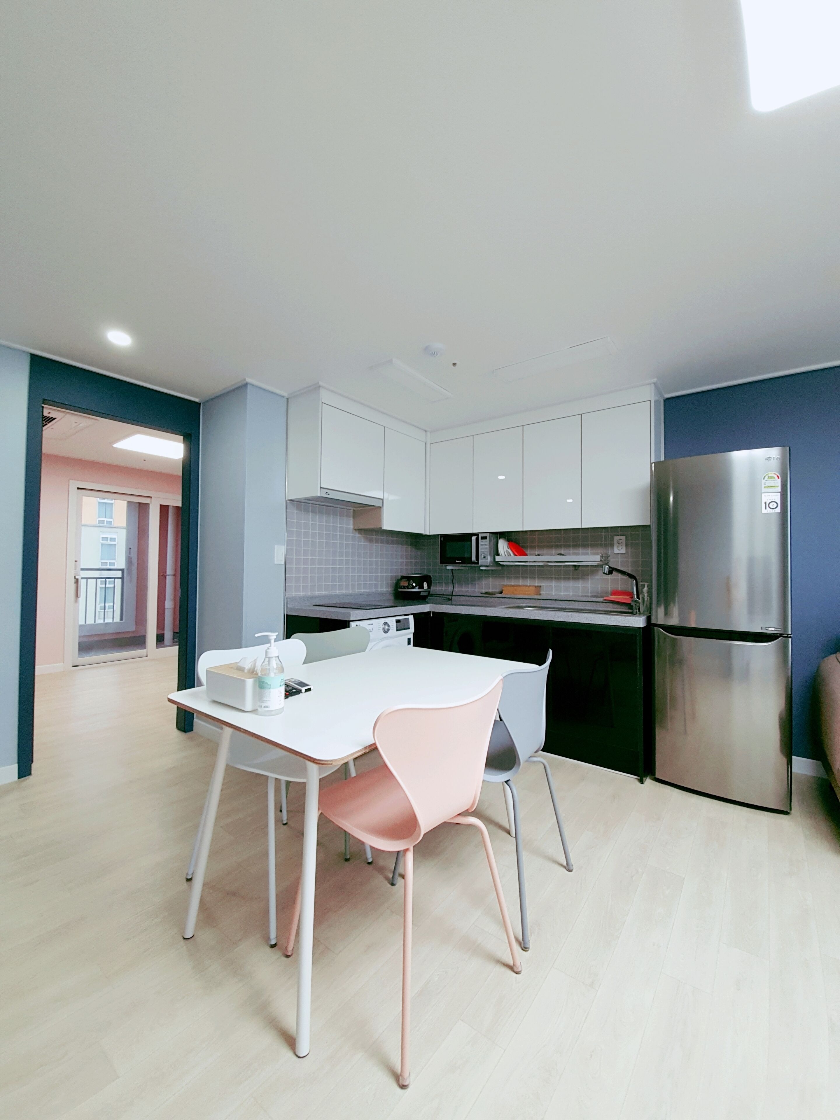 Una cocina moderna con armarios blancos, un refrigerador de acero inoxidable y un comedor con una mesa blanca y dos sillas.