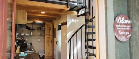 A modern kitchen with wooden cabinets, a stainless steel countertop, and a black staircase leading to an upper level.
