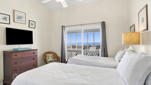 A hotel room with two beds, a TV on a dresser, a chair, a window with a view, and a ceiling fan. - Beachfront Retreat | Screened Porch | West Beach (Gulf Shores)