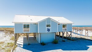 A beach house with a 'Howard Ranch' sign, wooden deck, and a view of the ocean. - Beachfront Retreat | Screened Porch | West Beach (Gulf Shores)