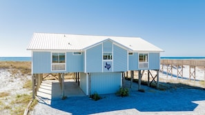 A beach house with a 'Howard Ranch' sign, wooden deck, and a view of the ocean.