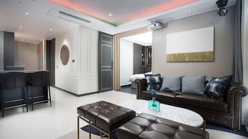 A modern living room with a brown leather sofa, a round coffee table, and a dining area with two black chairs.