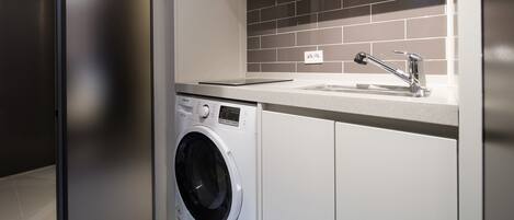 Une buanderie moderne équipée d’un lave-linge à chargement frontal, d’un évier et d’un pare-feu en carrelage.