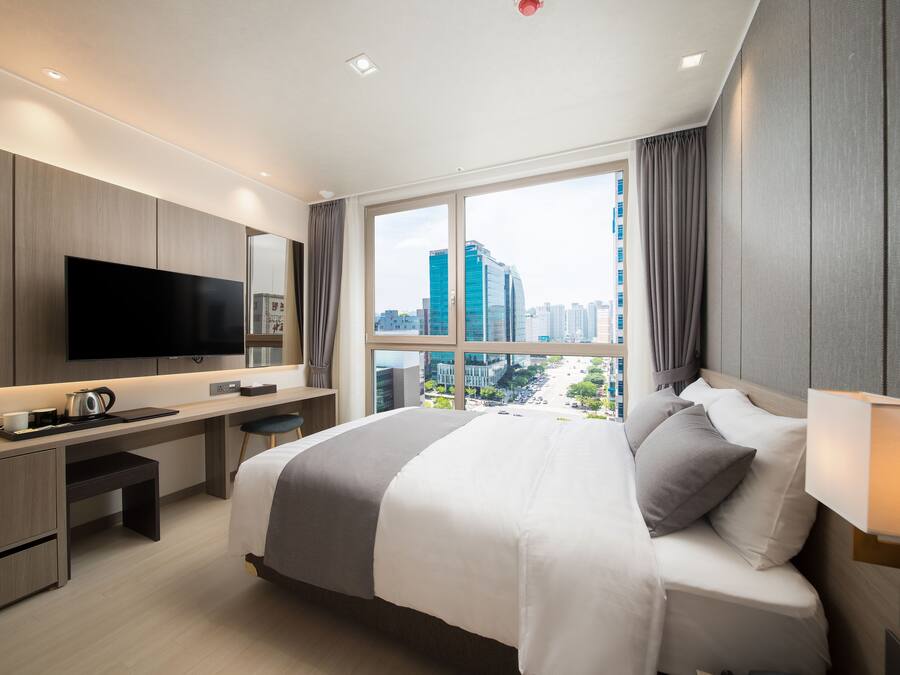 A modern hotel room with a large bed, a desk, a flat-screen TV, and a city view.