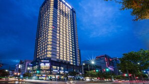Un hotel de gran altura con varios pisos, ventanas iluminadas y una entrada destacada a nivel de calle.