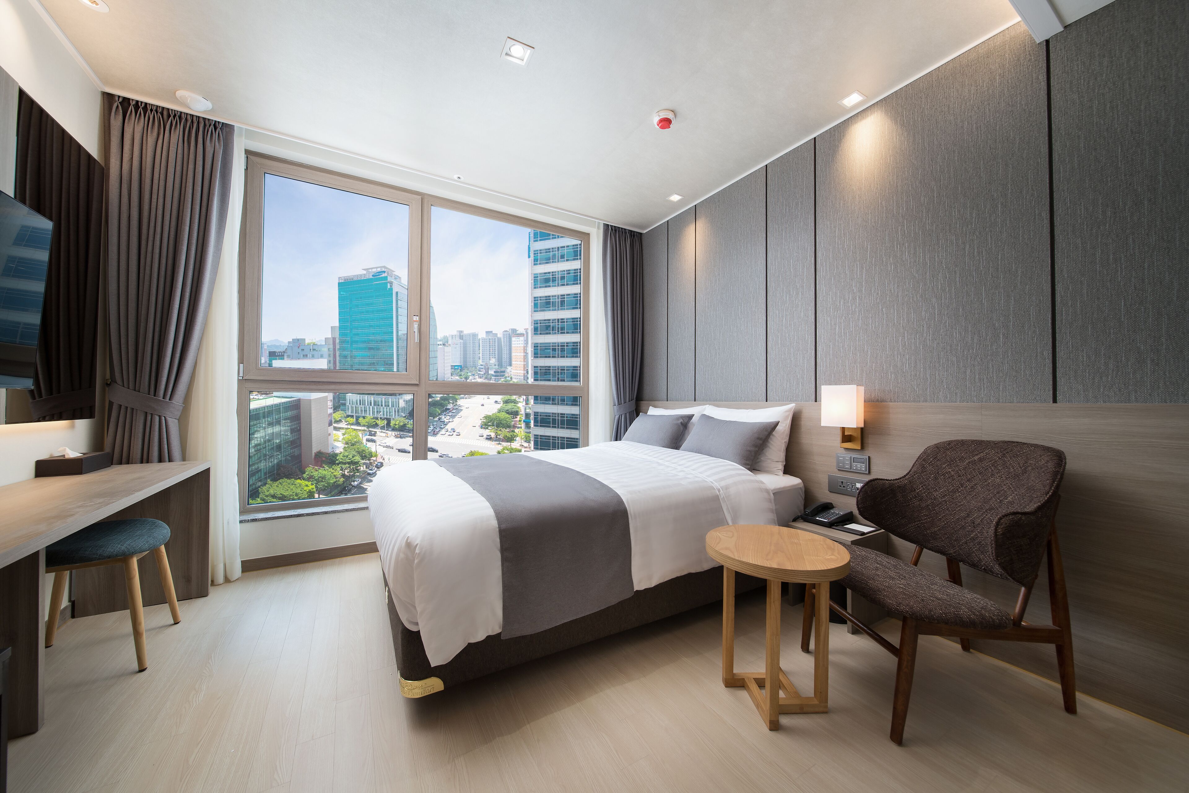 A modern hotel room with a large bed, a desk, a chair, and a view of the cityscape.
