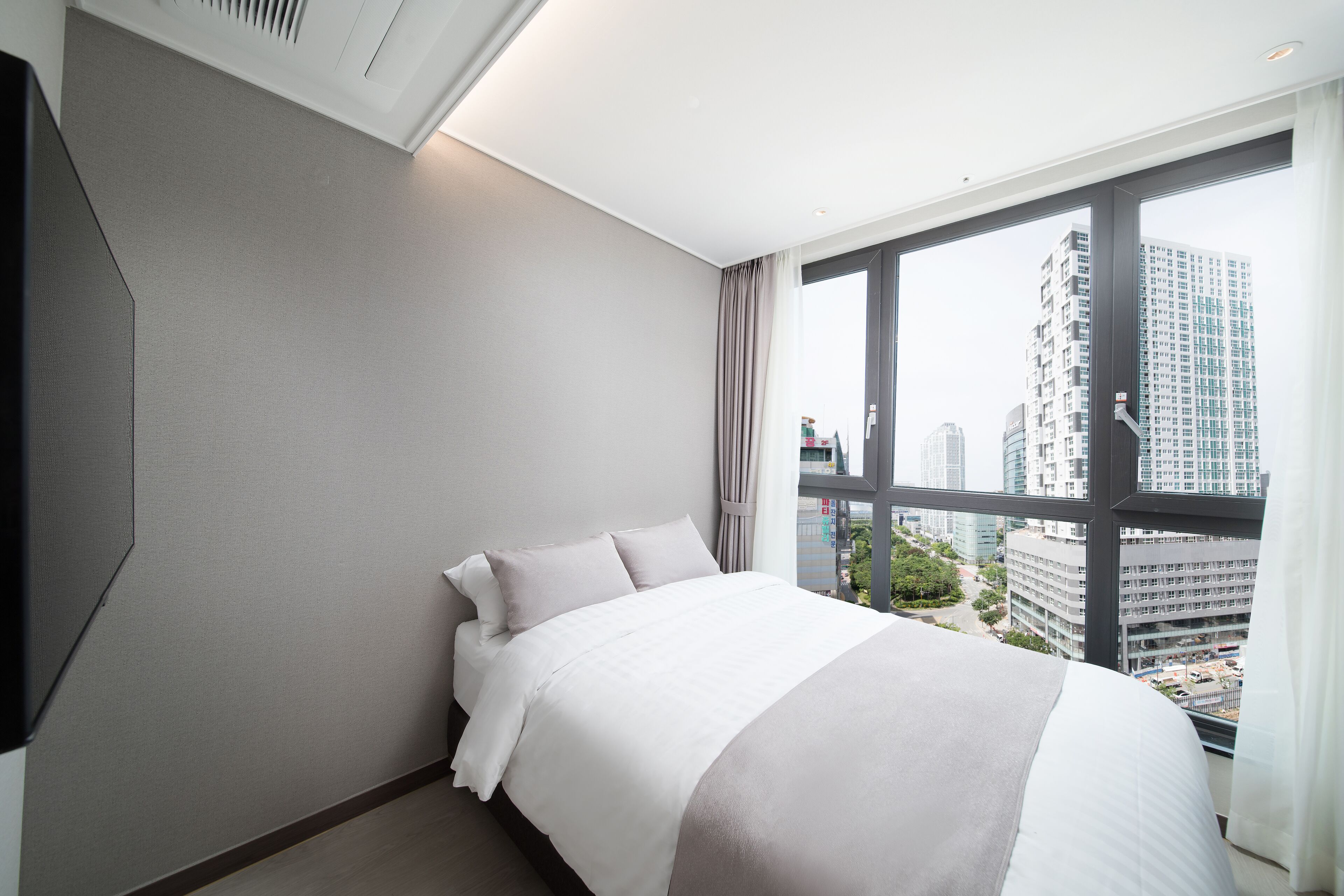 Une chambre d’hôtel moderne dotée d’un grand lit, offrant une vue sur la ville, et d’un téléviseur à écran plat fixé au mur.