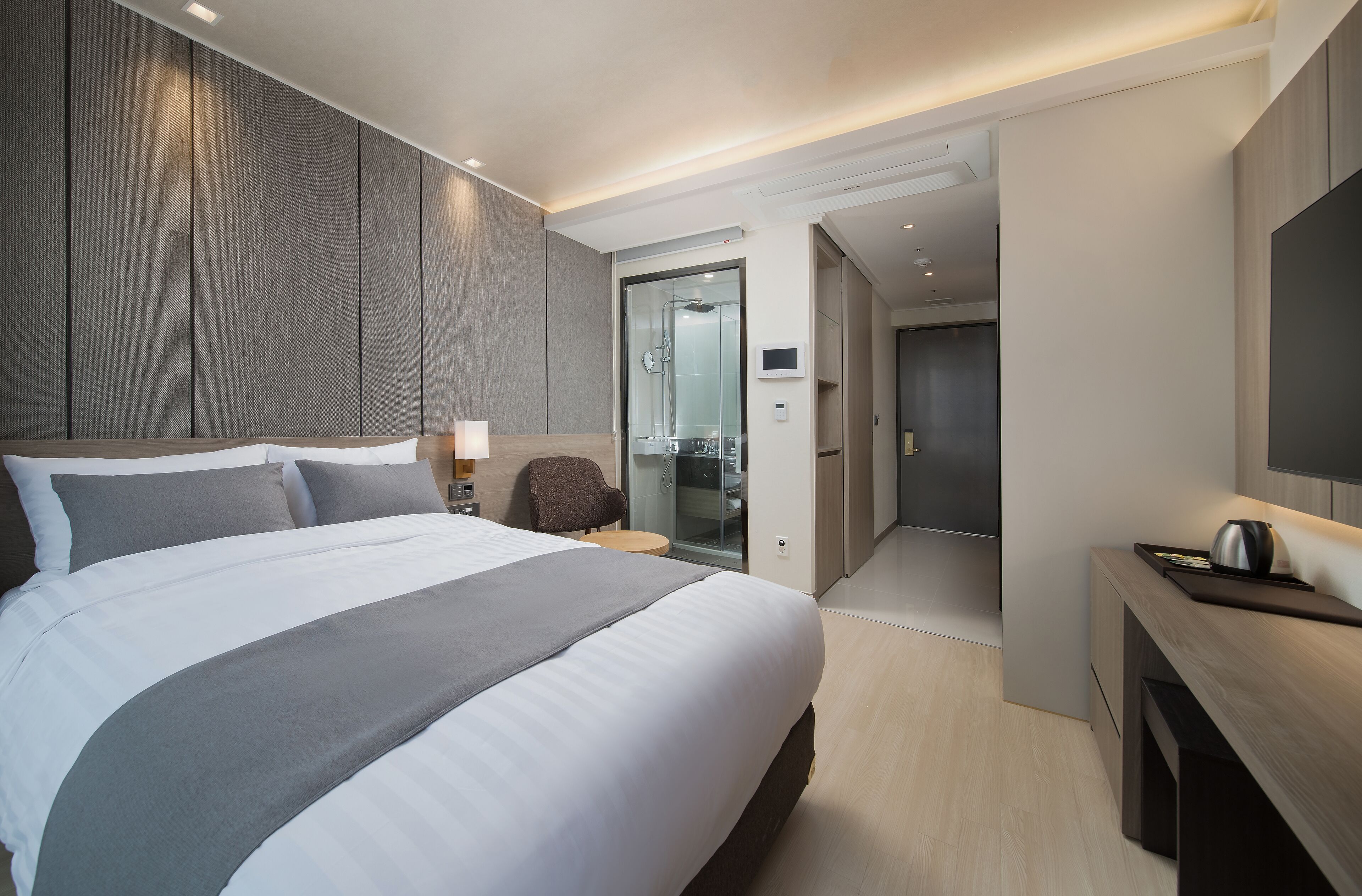 Habitación de hotel moderna con una cama grande, mesitas de noche, televisión y baño visible a través de una puerta de cristal.