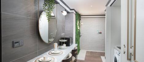 Un baño moderno con encimera de mármol, un espejo grande, lavadora integrada y una pared cubierta de plantas verdes.
