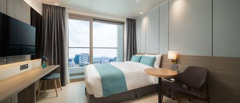 A modern hotel room with a large bed, a desk, a chair, a TV, and a city view.