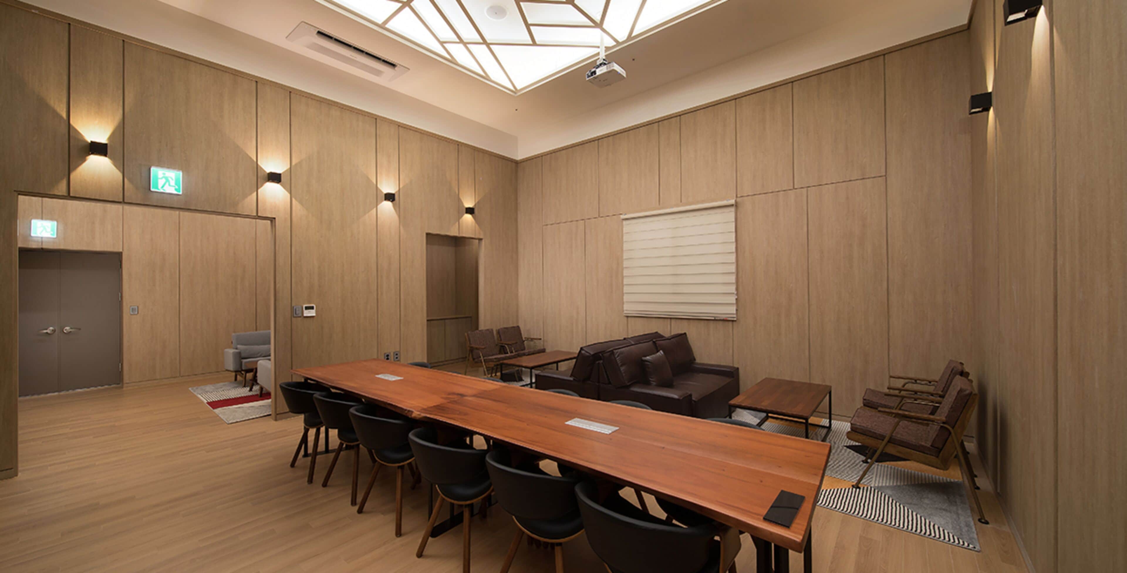 A conference room with a long wooden table, black chairs, a brown sofa, and a small coffee table.