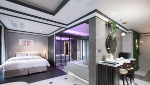 Una habitación de hotel moderna con una cama grande, una zona de estar, un baño con bañera y una kitchenette.