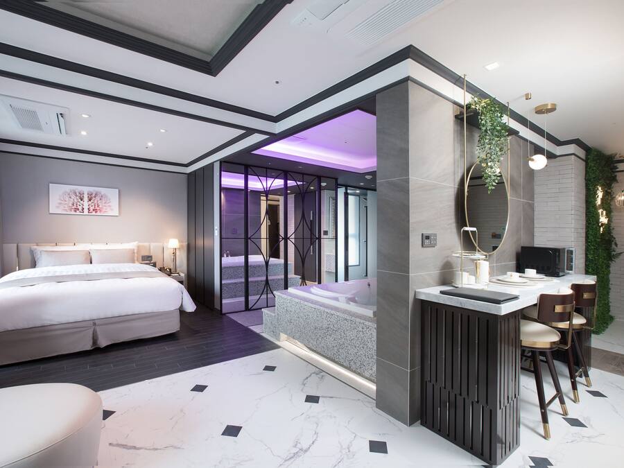 Une chambre d’hôtel moderne dotée d’un grand lit, d’un coin salon, d’une salle de bain avec baignoire et d’une kitchenette.