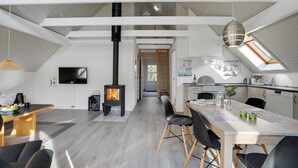 Una cocina moderna con estufa central, un comedor con mesa y sillas, y una escalera visible que conduce a un nivel superior.