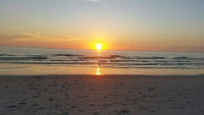 A beach with the sun setting over the horizon, reflecting on the water. - Marco Island Breeze in Naples (Naples)