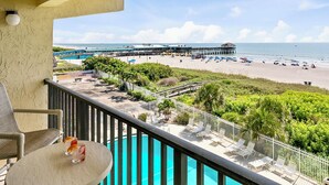 A balcony with a pool, overlooking a beach with umbrellas and lounge chairs. - Oceanview Condo w/ Balcony – Steps to Cocoa Beach Pier! (Cocoa Beach)