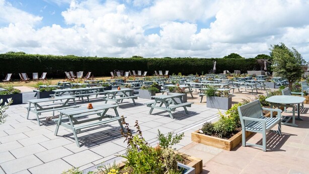 An outdoor patio area with numerous tables and chairs, surrounded by greenery and a hedge. - Queen s Hotel (Portsmouth)