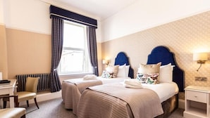 A hotel room with two beds, a desk, a chair, a radiator, and a window with curtains. - Queen s Hotel (Portsmouth)