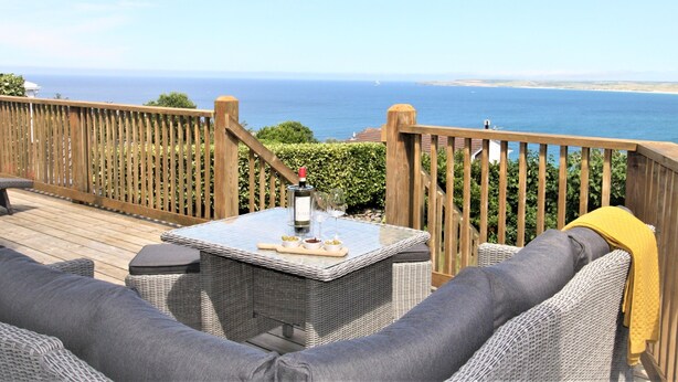 A deck with wicker furniture, a table with a bottle and glasses, and a view of the ocean.