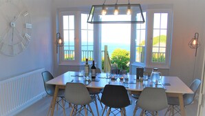 A dining area with a table set for four, large windows with a view, and a wall clock.