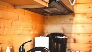 A wooden cabin interior with a black sink, a white bottle, and a black kettle on the counter. - Treehouse Place at Deer Ridge Ole Mill (Snohomish)