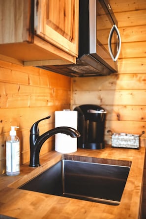 A wooden cabin interior with a black sink, a white bottle, and a black kettle on the counter.