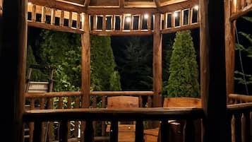 A wooden gazebo with a roof, surrounded by a wooden deck and chairs.