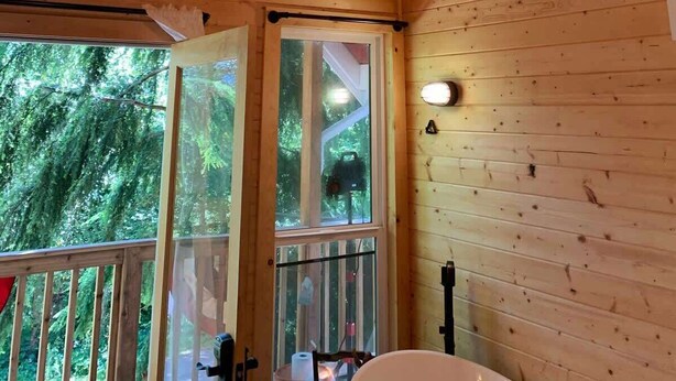 A wooden cabin interior with a hanging lantern, large windows, and a deck area. - Treehouse Place at Deer Ridge Ole Mill (Snohomish)