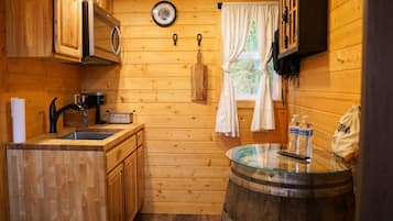 A compact kitchen with wooden cabinets, a sink, a microwave, and a window with curtains.