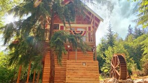 A wooden cabin with a balcony, surrounded by trees and a water wheel. - Treehouse Place at Deer Ridge Ole Mill (Snohomish)