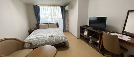 A hotel room with a bed, a desk with a TV, a chair, and a small table.